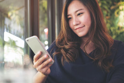 Close-up of woman using mobile phone sitting by window