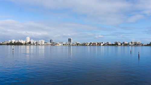 Sea by buildings in city against sky