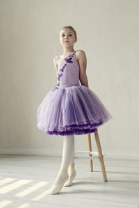 A portraits of a ballerina girl in a lilac dress posing in a room showing ballet poses