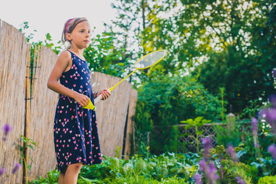 Girl playing badminton while standing by flowering plants