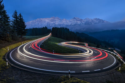 Light trail of moving cars driving up a panoramic serpentine road in the swiss alps 