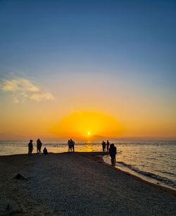 Silhouette people on beach against sky during sunset