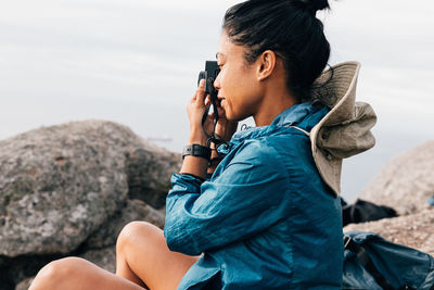 Woman photographing while sitting on rock