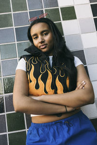 Portrait of teenage girl standing with arms crossed against tiled wall