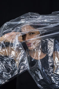 Model portrait with clear plastic in front of her face against black background. 