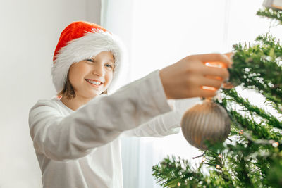 Happy teenage girl decorates the christmas tree at home on the eve of the holidays. 