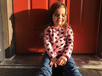 Girl smiling while sitting against closed red door