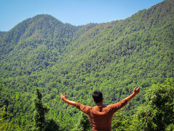 Rear view of man with arms raised against mountains