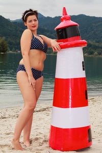Portrait of mid adult woman in swimwear standing by toy lighthouse at lakeshore