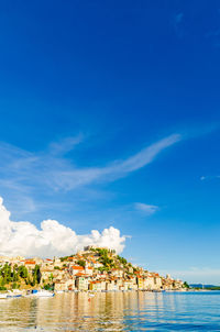 Buildings by sea against blue sky