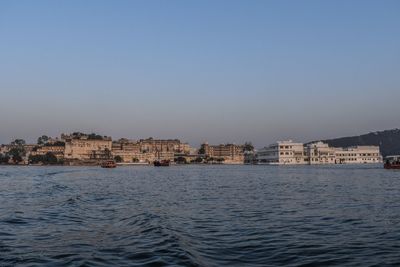 Buildings by lake against clear blue sky