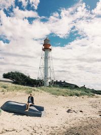 Young woman sitting on boat at beach against lighthouse