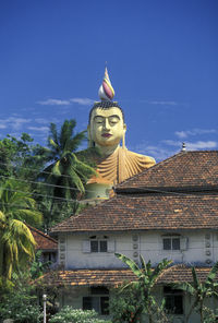 Low angle view of giant buddha statue by building against blue sky