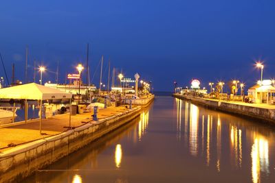 Boats in river by illuminated city against sky at night