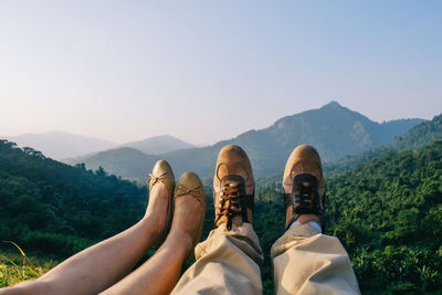 Low section of people relaxing on mountain against clear sky