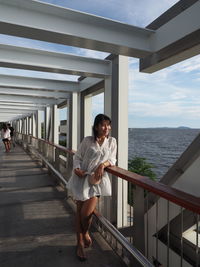 Full length of woman standing on railing against sea