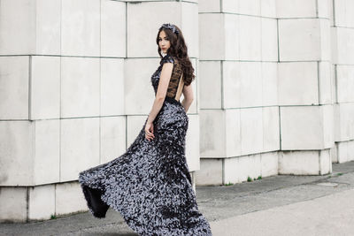 Portrait of beautiful woman wearing evening gown while posing against wall