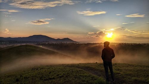 Rear view of man standing on land against sky during sunset