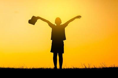 Silhouette woman standing on field against sky during sunset