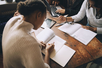 High angle view of friends studying at table while sitting in room