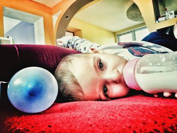 Portrait of cute baby girl drinking milk while lying at home