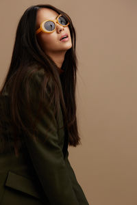 Portrait of young woman wearing sunglasses while standing against wall