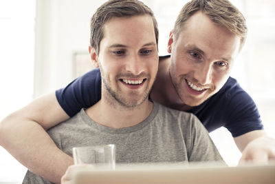 Happy homosexual couple using laptop while embracing at home