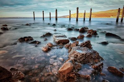 Wooden posts in sea against sky