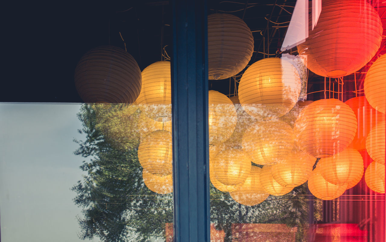 LOW ANGLE VIEW OF ILLUMINATED LANTERNS HANGING ON GLASS WALL