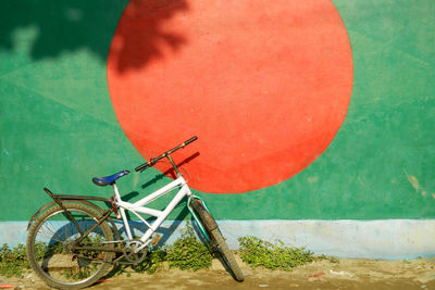 Bicycle parked against flag of bangladesh painted on wall