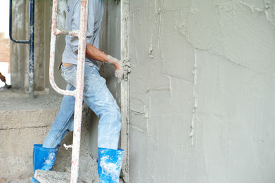 Selective focus on the surface of cement wall with blurred hands of worker plastering background