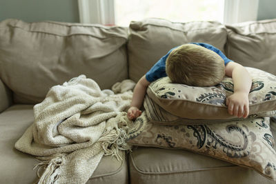 Tired young child asleep at home on couch lying on stacked pillows
