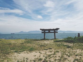 Abandoned torii gate on field by sea against sky