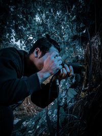 Portrait of young man holding camera in forest