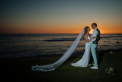 Bride and groom  by sea against sky during sunset