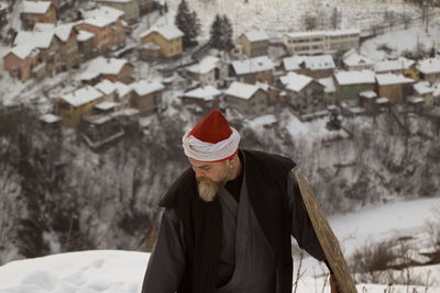 Midsection of person with umbrella on snow against buildings