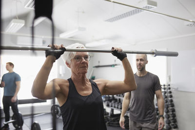 Senior woman lifting barbell pole in gym