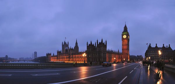 Illuminated big ben by road against cloudy sky at dusk