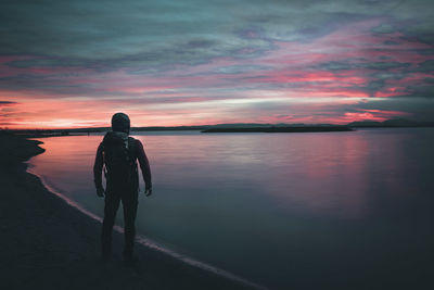 Rear view of man standing by sea against sky during sunset
