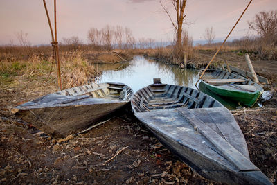 Abandoned boat moored on field by lake against sky