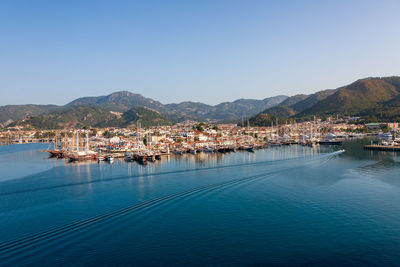 Sailboats in city by sea against clear blue sky