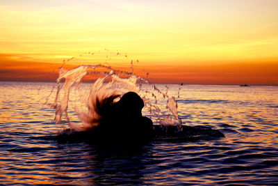 Silhouette woman tossing hair in sea against sky during sunset