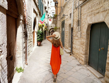 Woman with long orange summer dress walking in narrow alley of bisceglie, apulia, italy