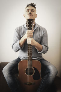 Man holding guitar while sitting by wall