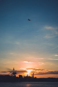Airplane flying over sea against sky during sunset