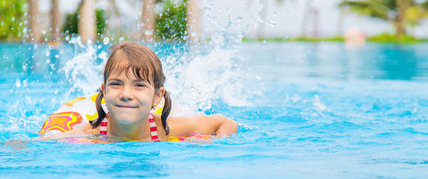 Portrait of girl splashing water while swimming in pool