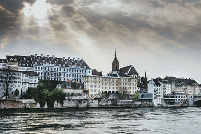 River by buildings in city against cloudy sky