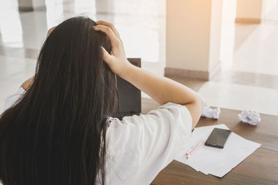 Rear view of woman using phone on table