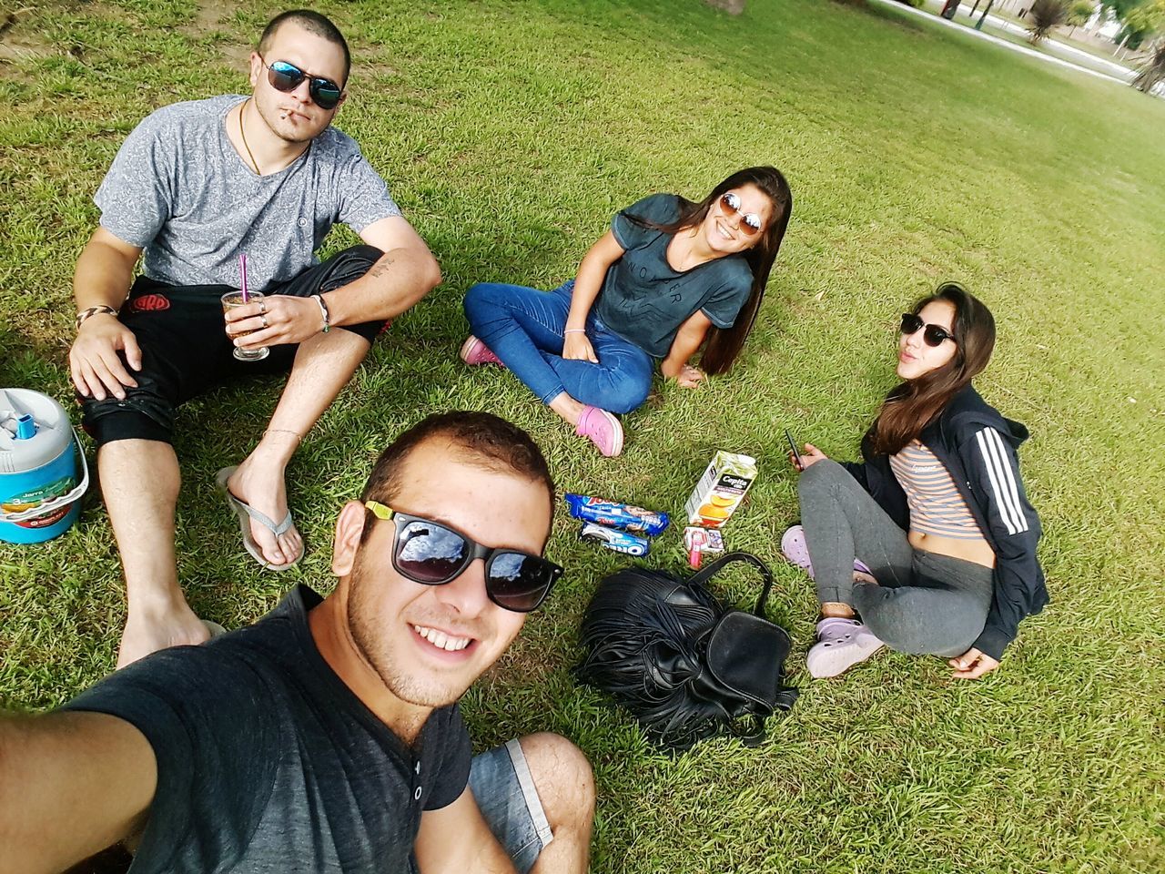 sunglasses, grass, friendship, high angle view, young adult, wireless technology, casual clothing, lying down, portable information device, sitting, relaxation, young men, young women, happiness, outdoors, mobile phone, day, togetherness, real people, technology, portrait, looking at camera, people, smiling, adult, adults only