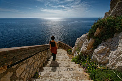 Rear view of woman moving down on steps against sea